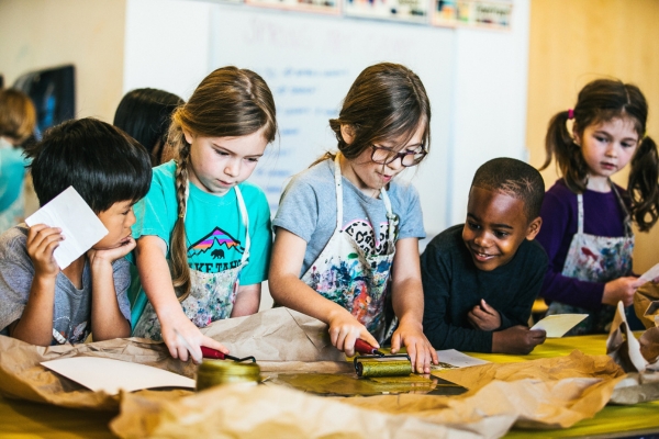 two children practice printmaking while other excitedly watch