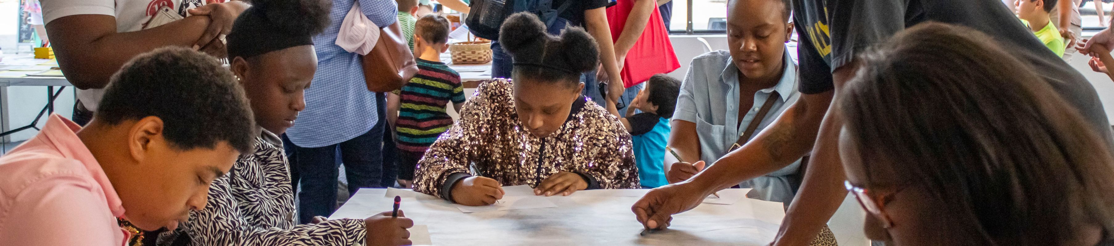 a family sits and stands around a table working on a group art project