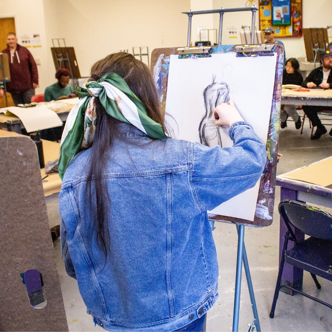 Young woman standing at an easel drawing a figure