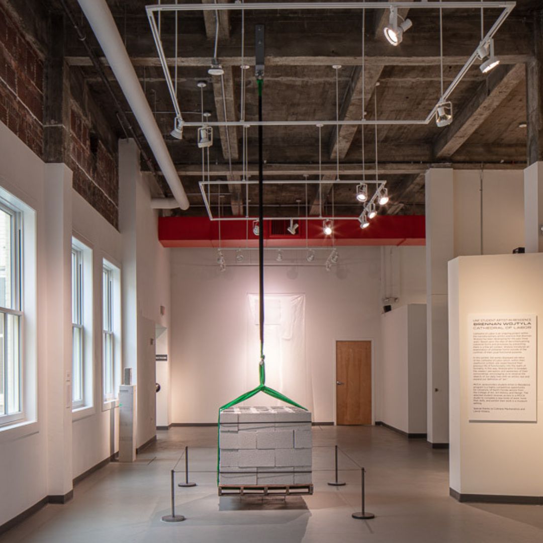 one ton of cinder blocks stacked on a wood pallet hangs from the museum ceiling