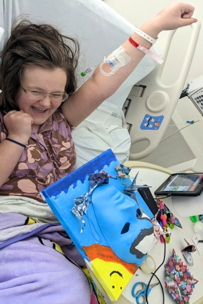 child posing with their artwork, smiling and posing with arm up as though they are flying