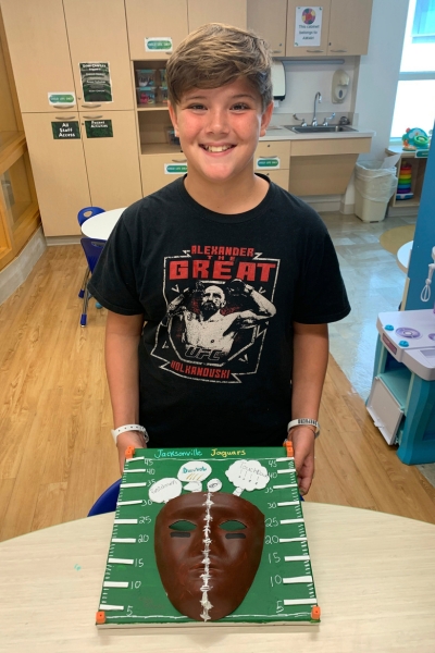 child smiling and posing with their artwork, which features a football field 