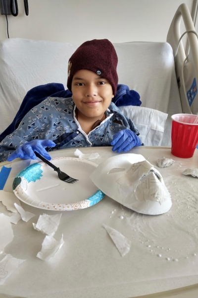 child smiling and posing with their artwork, which features paper mache 