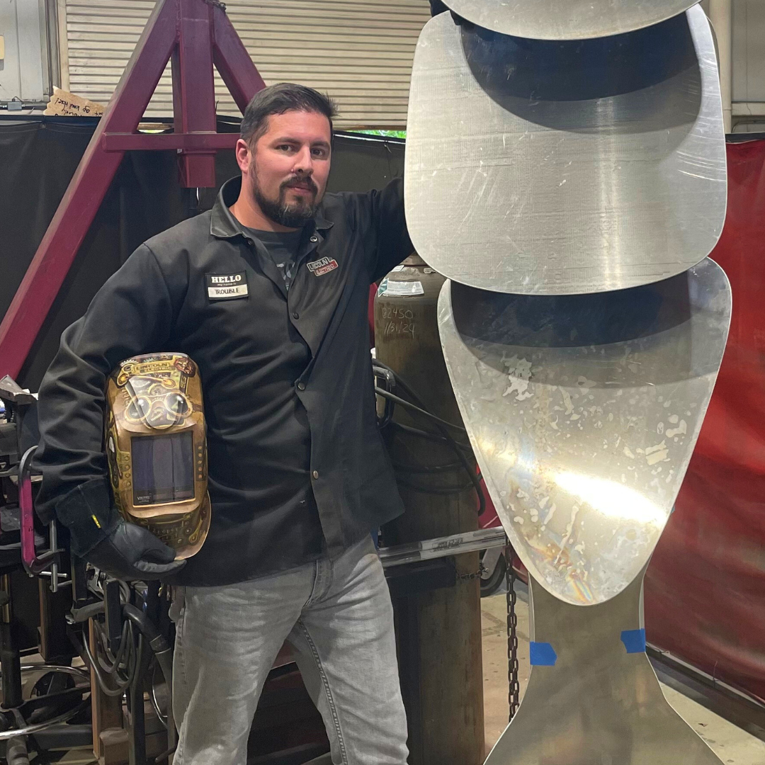 profile picture of UNF Student Artist-in-Residence Dustin Sims standing next to one of his large scale sculptures